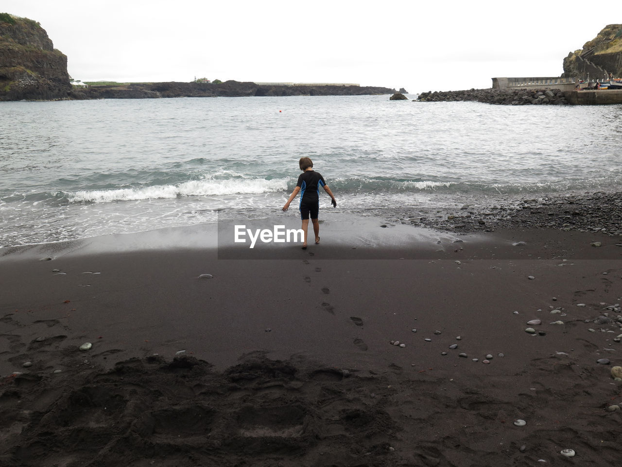 Rear view of girl standing on beach against sky