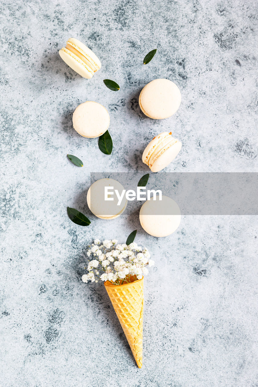 Waffle cone filled with gypsophila flowers and macarons with leaves. pastel colors.