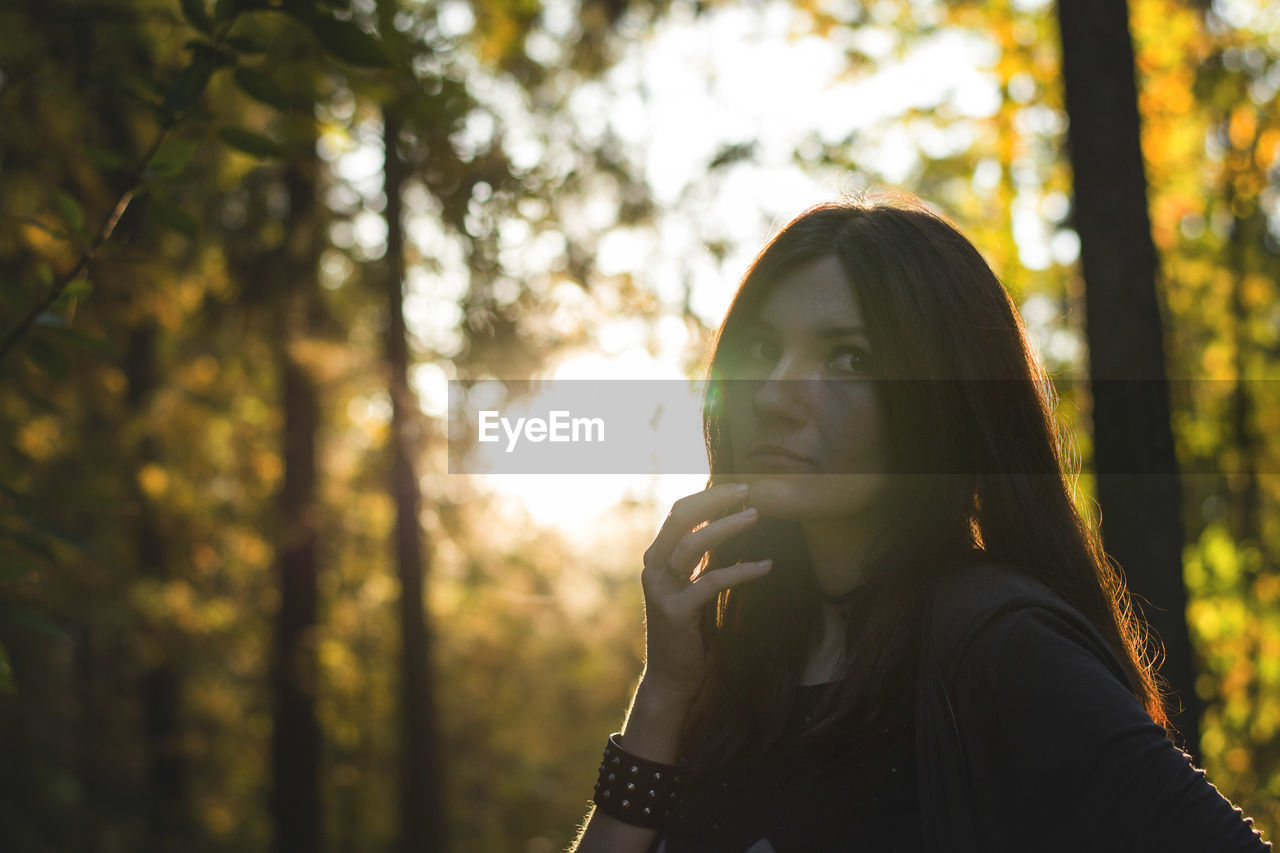 Thoughtful young woman against trees in forest