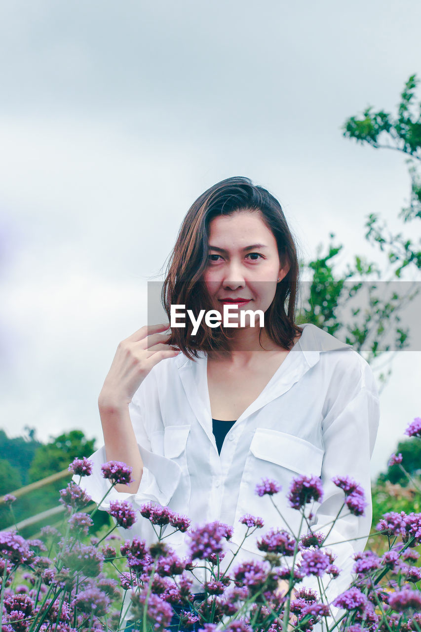 PORTRAIT OF A BEAUTIFUL YOUNG WOMAN STANDING BY PURPLE FLOWER