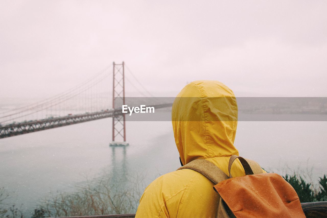 Rear view of young man looking at golden gate bridge over bay against sky