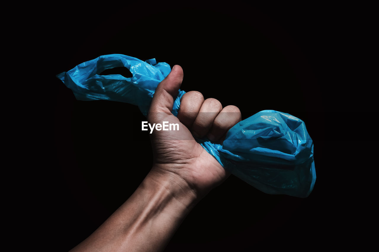 Close-up of human hand holding plastic against black background