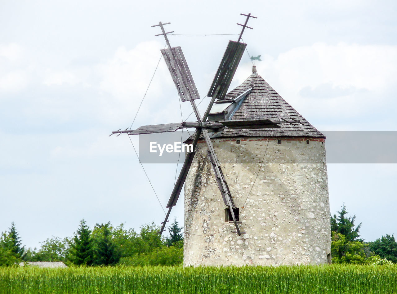 Windmill on field against cloudy sky