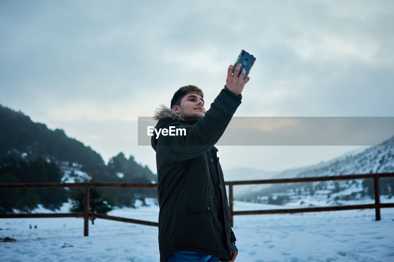 A young man takes a selfie with his mobile phone on a snowy day