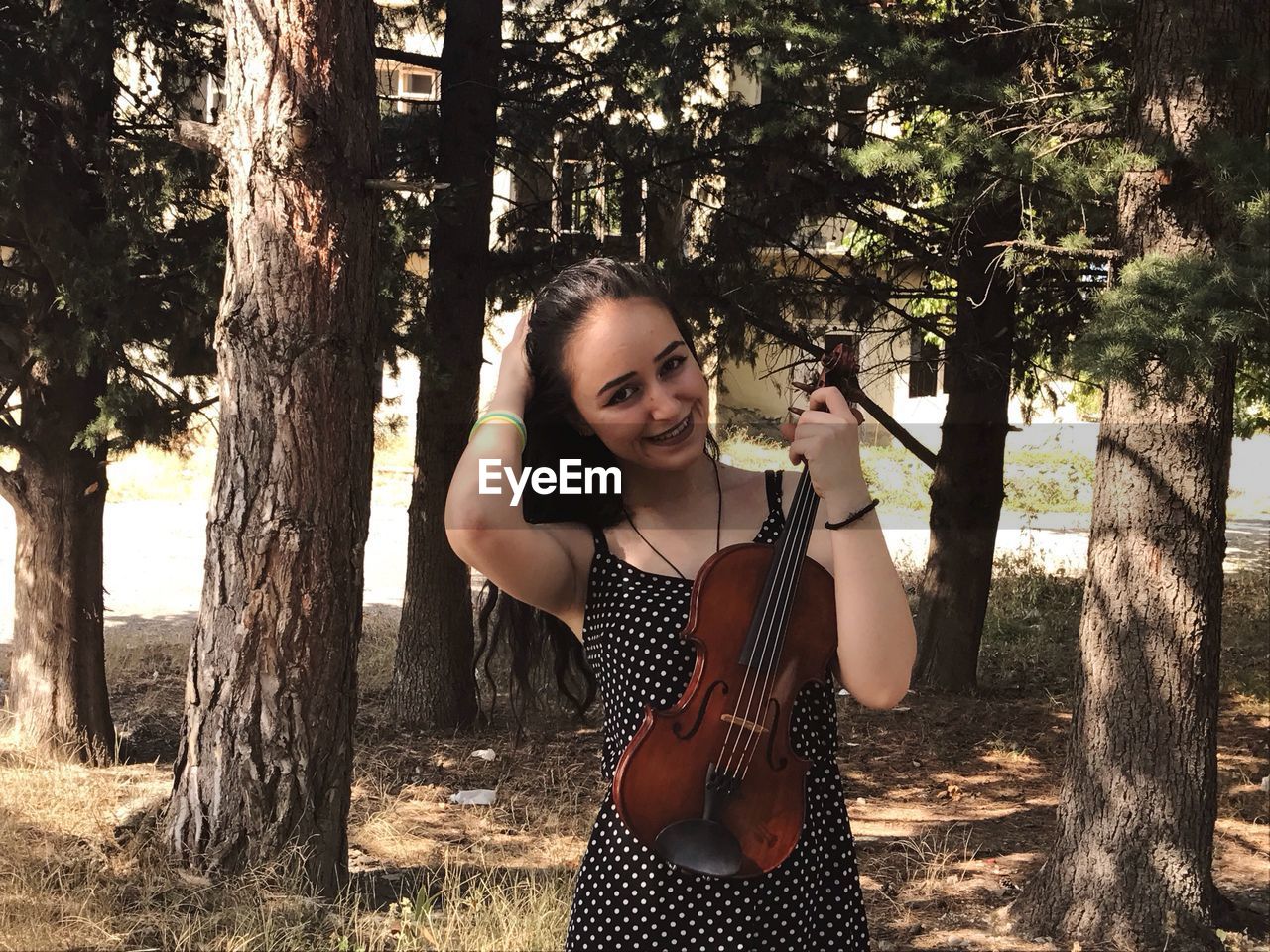 Portrait of beautiful woman holding violin against trees