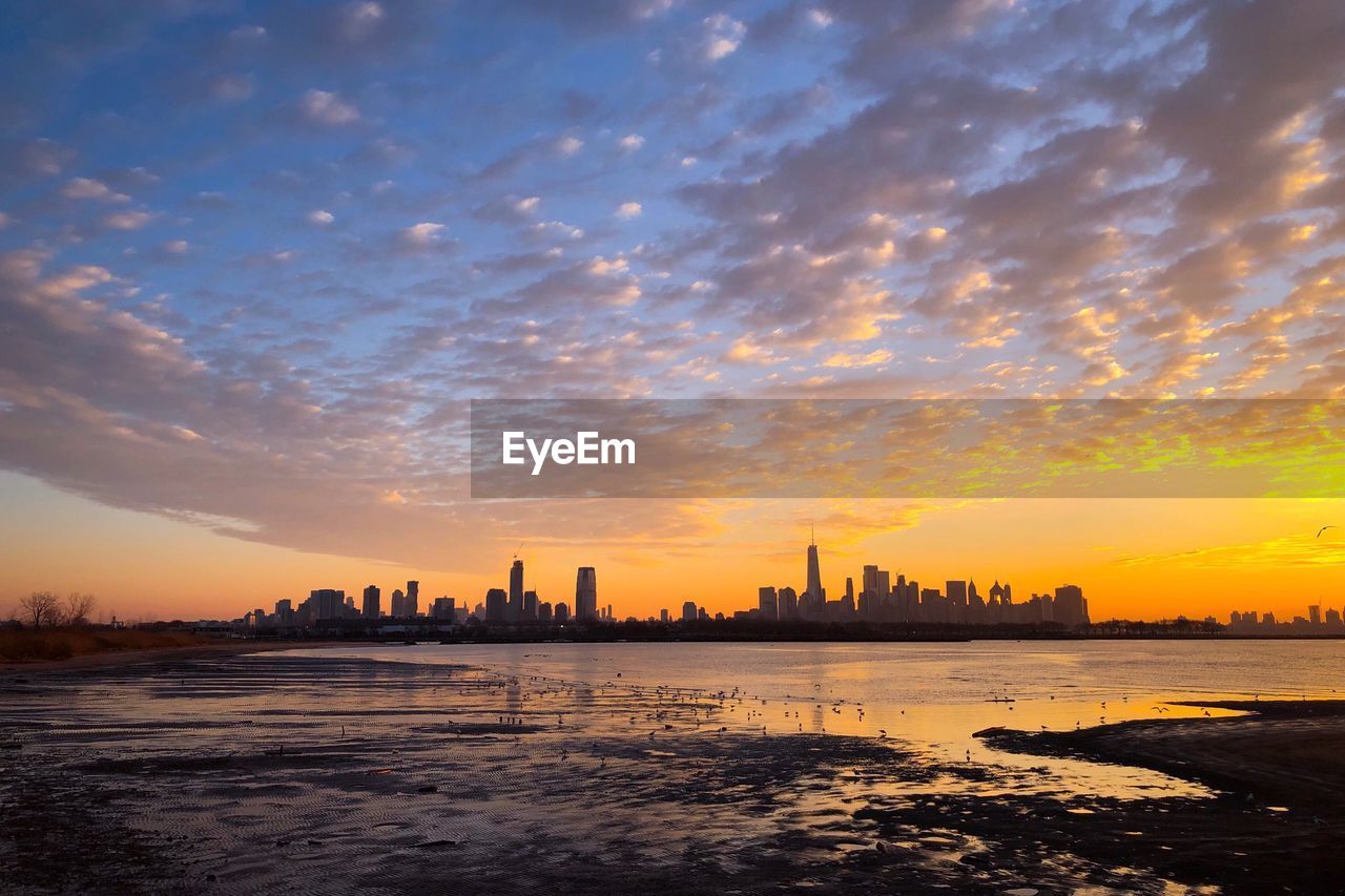 Silhouette buildings by city against sky during sunset