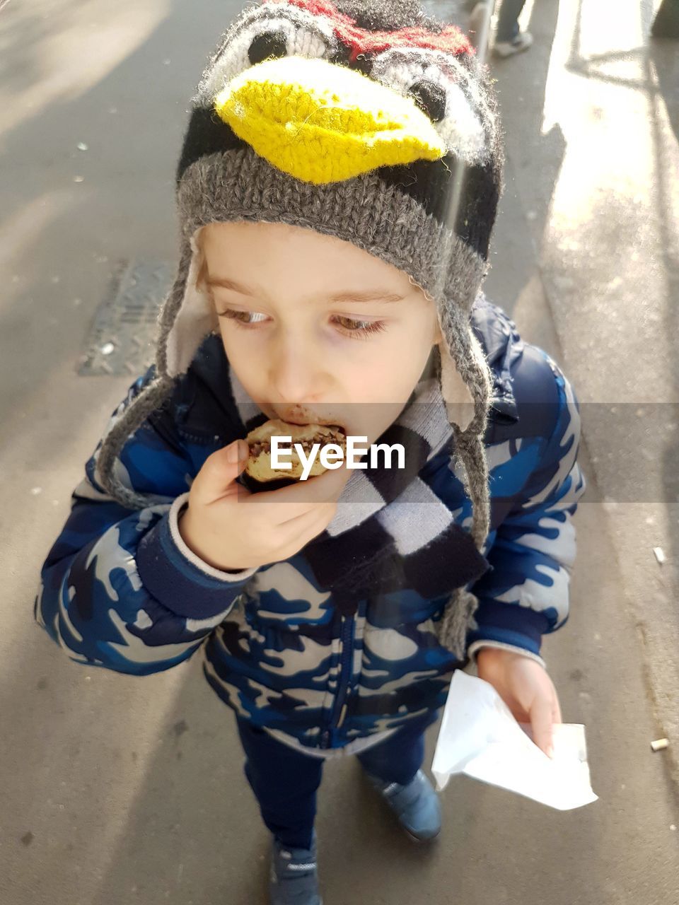 High angle view of boy eating food while standing on road