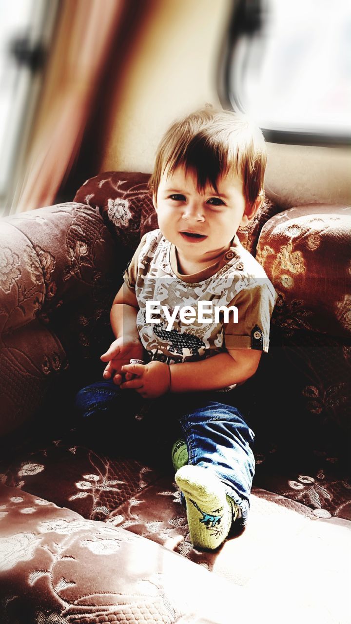 High angle portrait of cute baby boy sitting on sofa at home