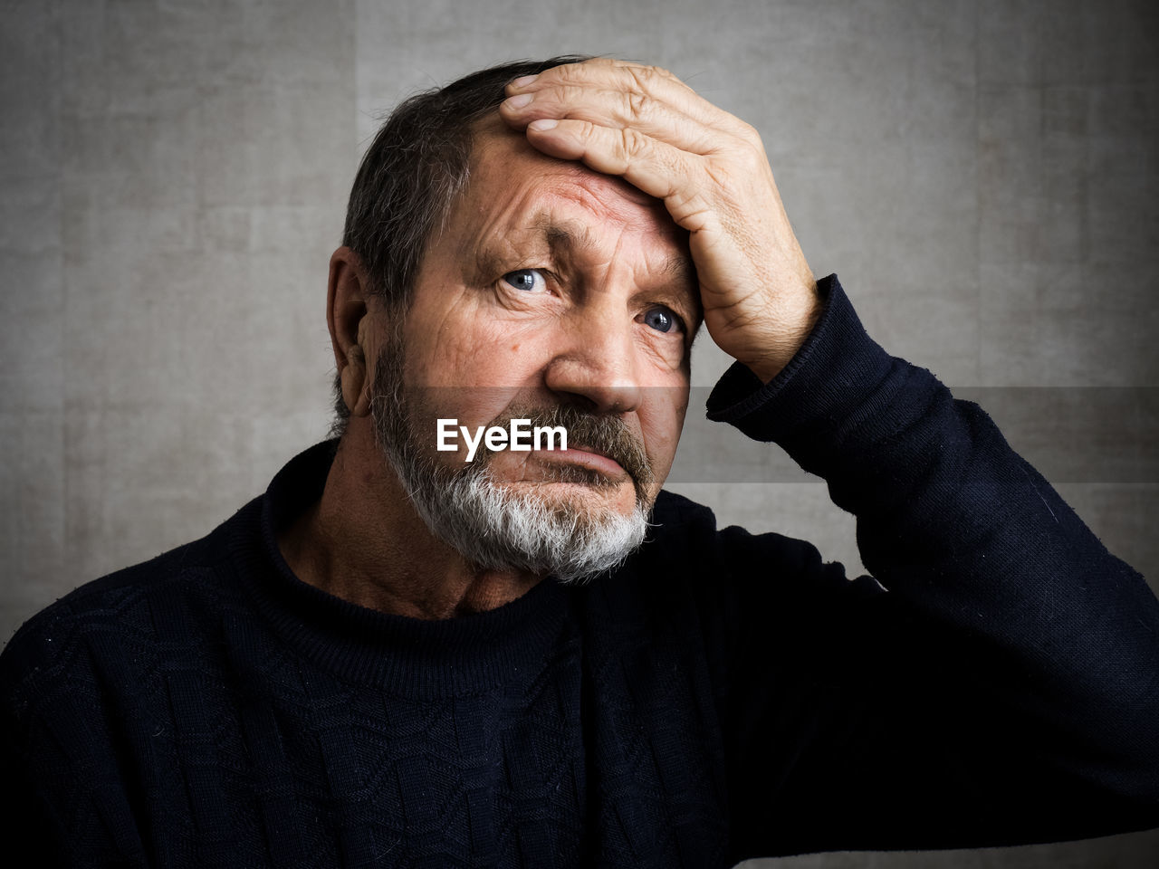 Thoughtful man with head in hands against wall