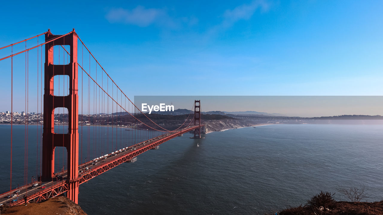 architecture, sky, travel destinations, built structure, suspension bridge, water, bridge, transportation, travel, nature, tourism, bay, city, sea, bay of water, landscape, scenics - nature, cloud, beauty in nature, engineering, environment, urban skyline, cityscape, panoramic, tranquility, building exterior, blue, fog, red, tranquil scene, outdoors, copy space, land, dusk, beach, twilight, road, building, coastline, reflection, horizon, sunset, city life, mountain, sunlight, motion, dramatic sky, holiday, mode of transportation, long exposure, summer, aerial view, trip, illuminated, vacation, awe, idyllic, day, cloudscape, water's edge, business finance and industry, cable-stayed bridge, sun, traffic, street