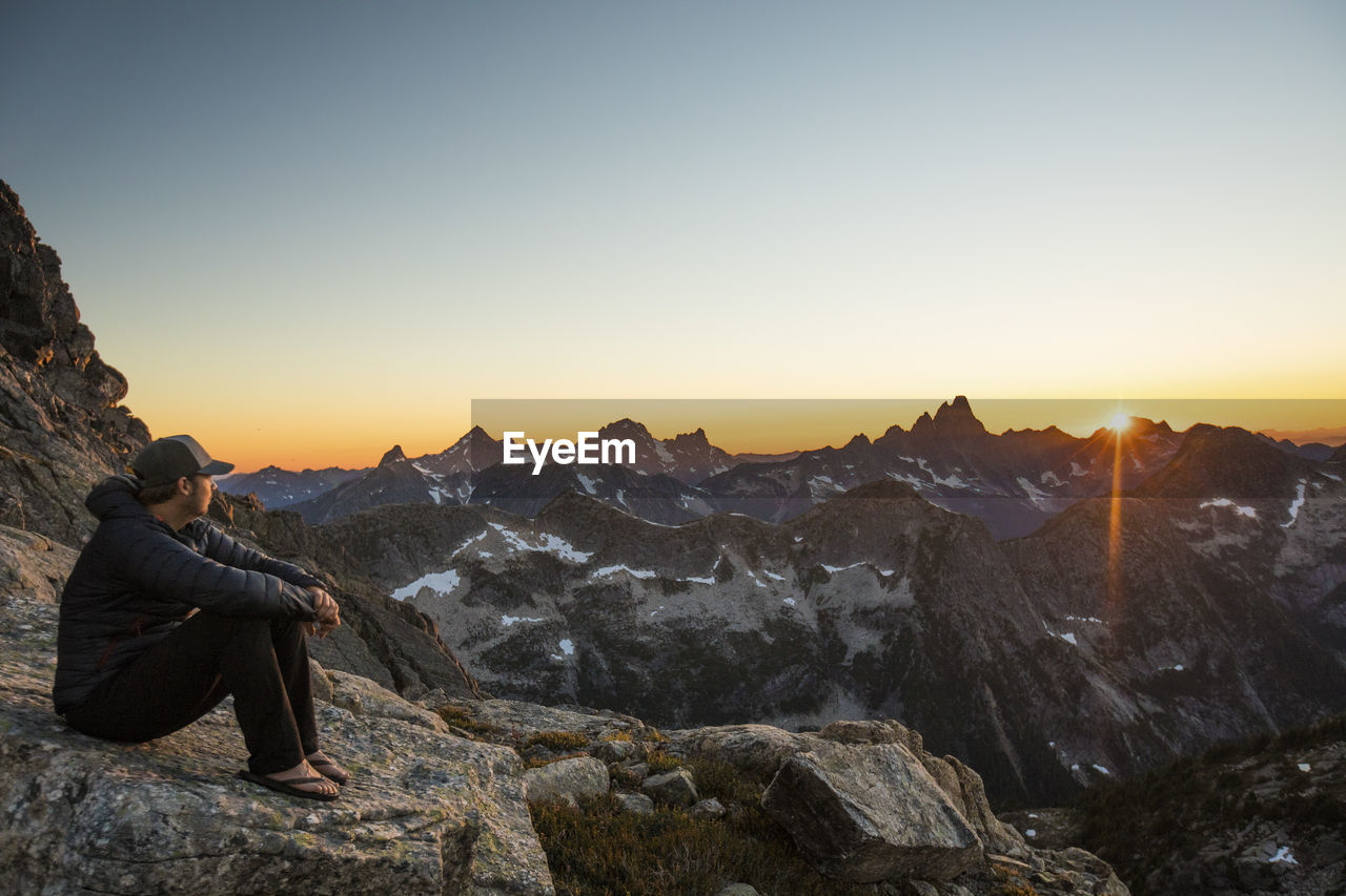 Active fit man resting on rock in mountains watching sunset.