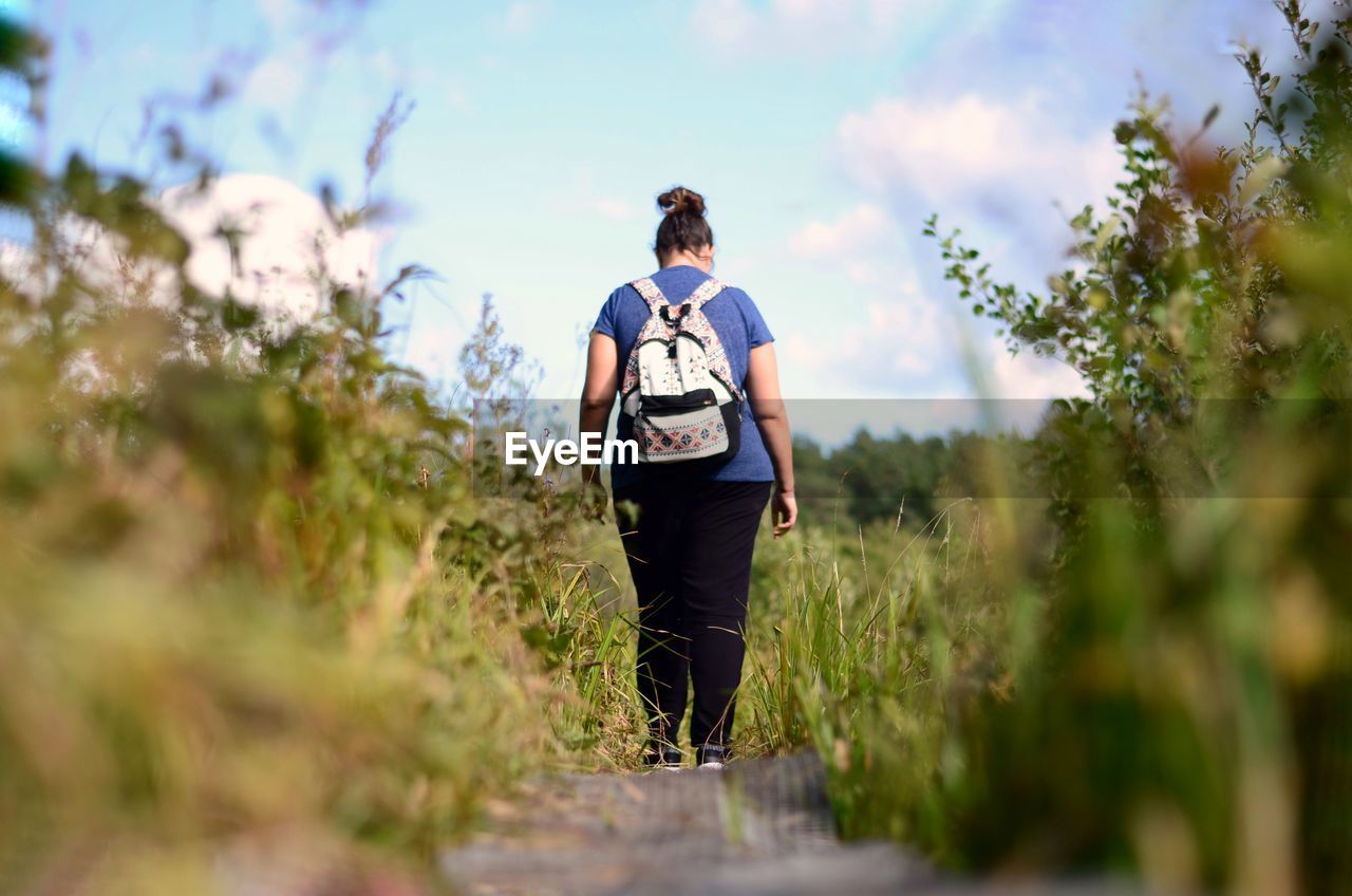 Rear view of woman walking on field against sky