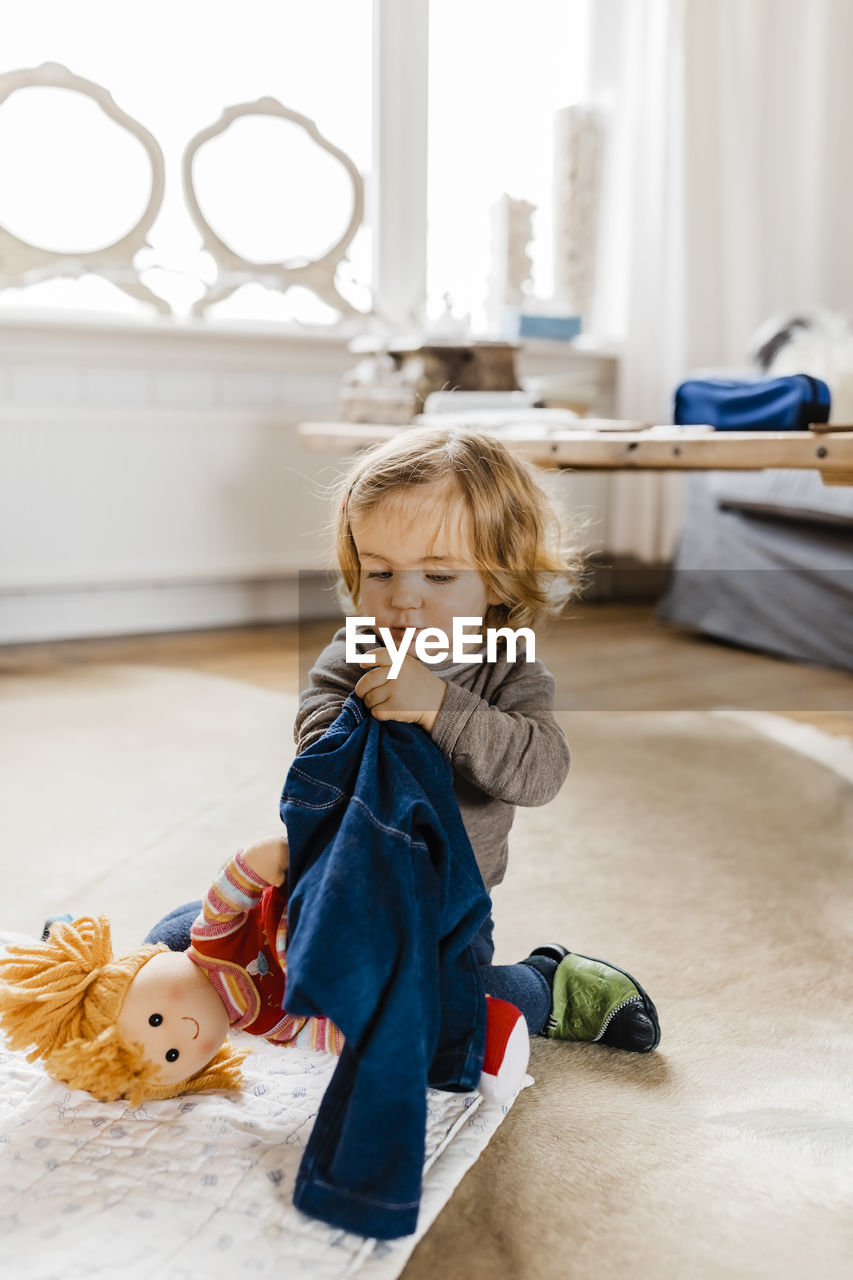 Cute girl playing with doll while sitting on carpet at home