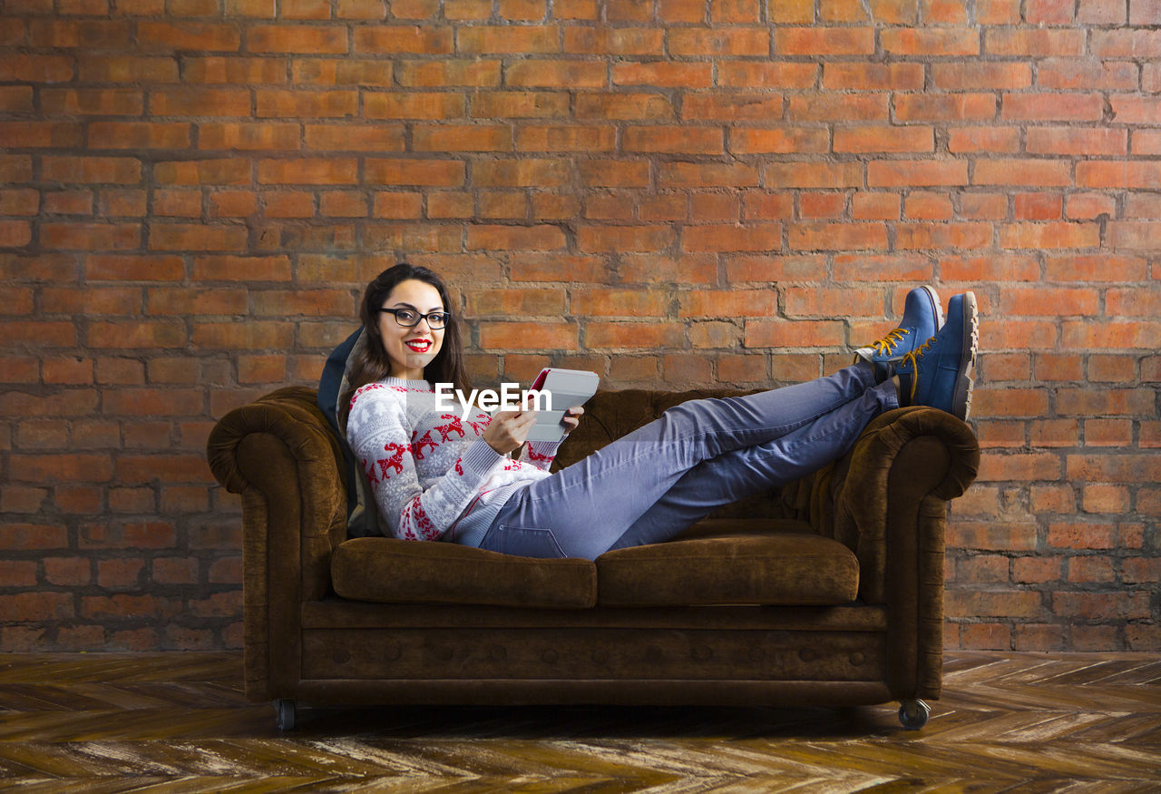 FULL LENGTH OF YOUNG WOMAN SITTING ON BRICK WALL