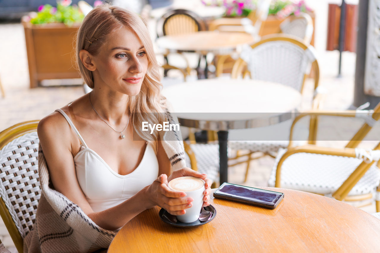 Beautiful young woman in warm plaid in an outdoor cafe at table drinking