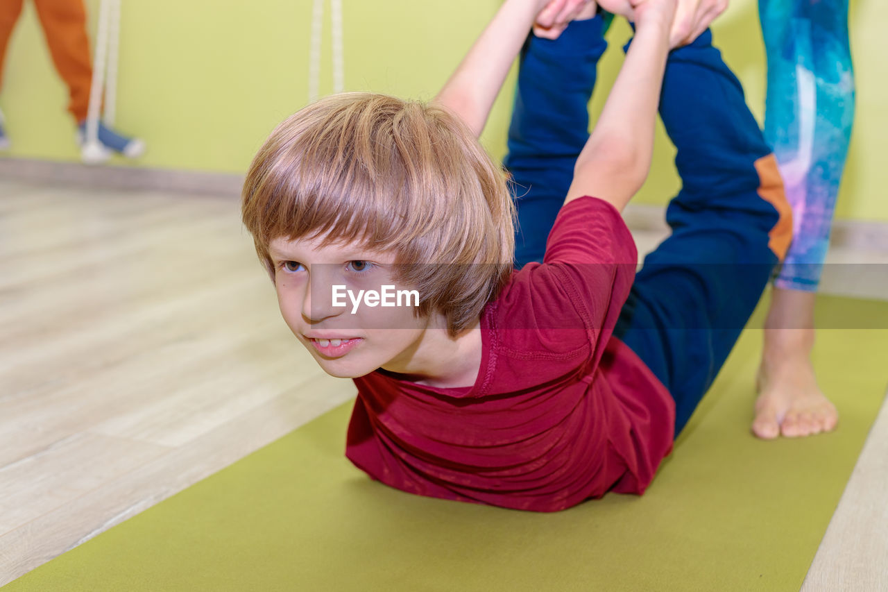 A woman instructor in a sports uniform is engaged in yoga with a boy. 