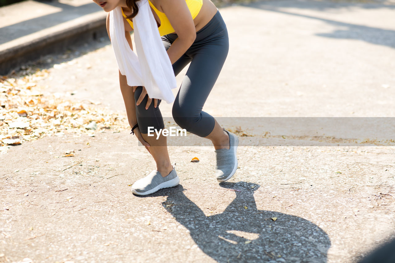 LOW SECTION OF WOMAN STANDING ON FOOTPATH WITH SHADOW