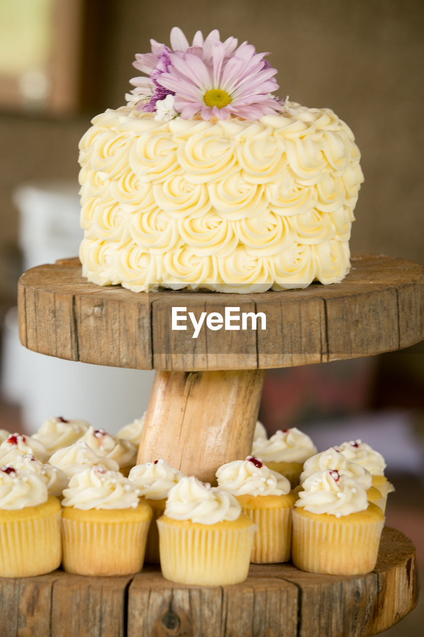 Close-up of wedding cake and cupcakes on wooden stand