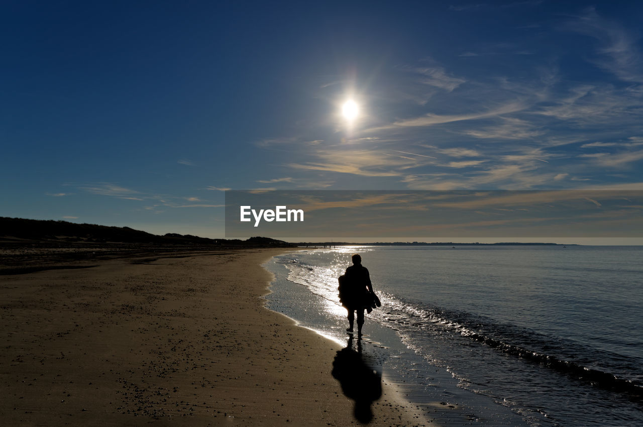 Rear view of silhouette man on beach against sky during sunset