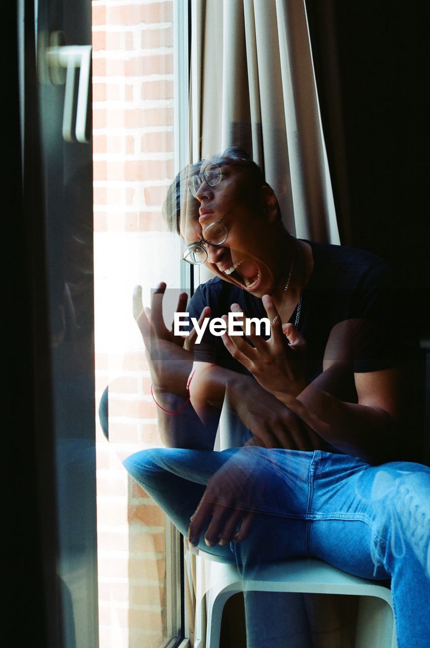 Double exposure of man sitting by window at home