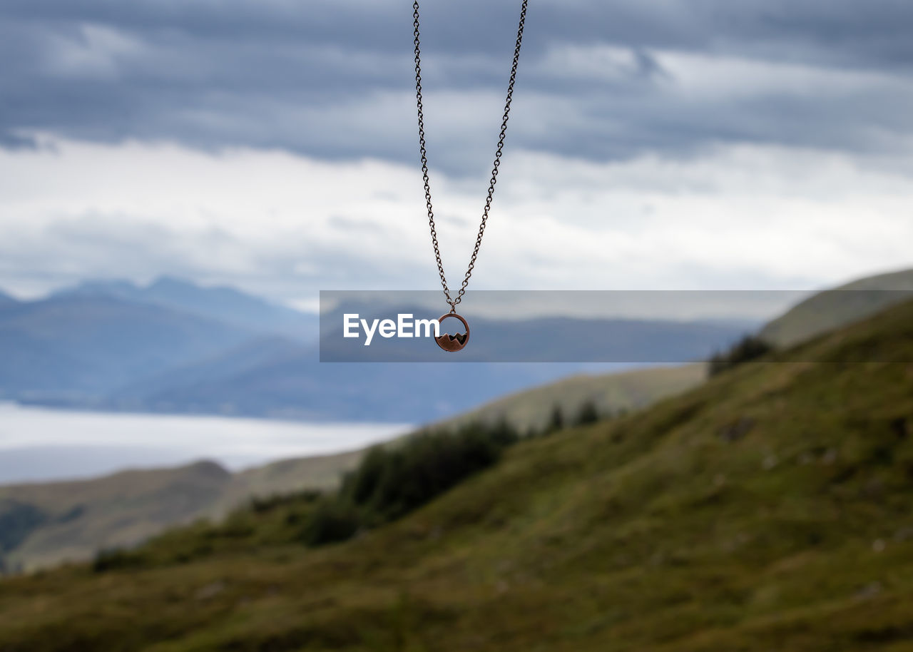 Necklace with mountains on it hanging in front of mountains by norwegian fjord. 