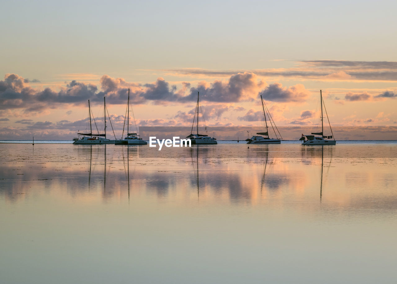 Sailboats in sea at sunset