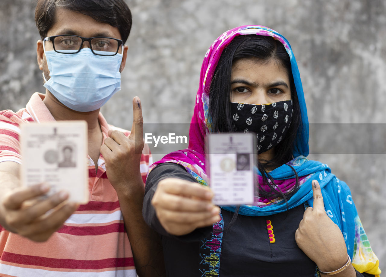 A man and woman showing ink-marked finger and voter card with safety nose mask on