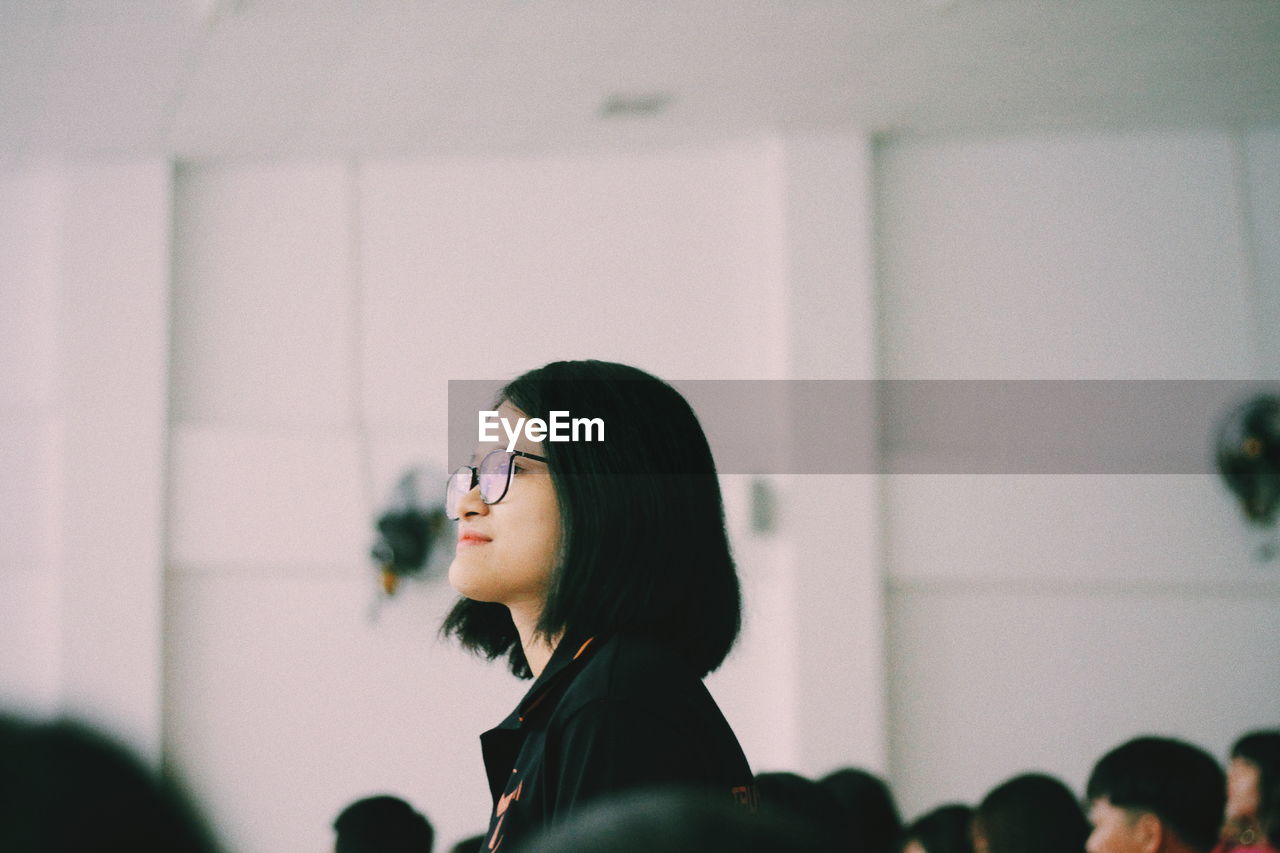 Side view of woman wearing eyeglasses while standing against wall