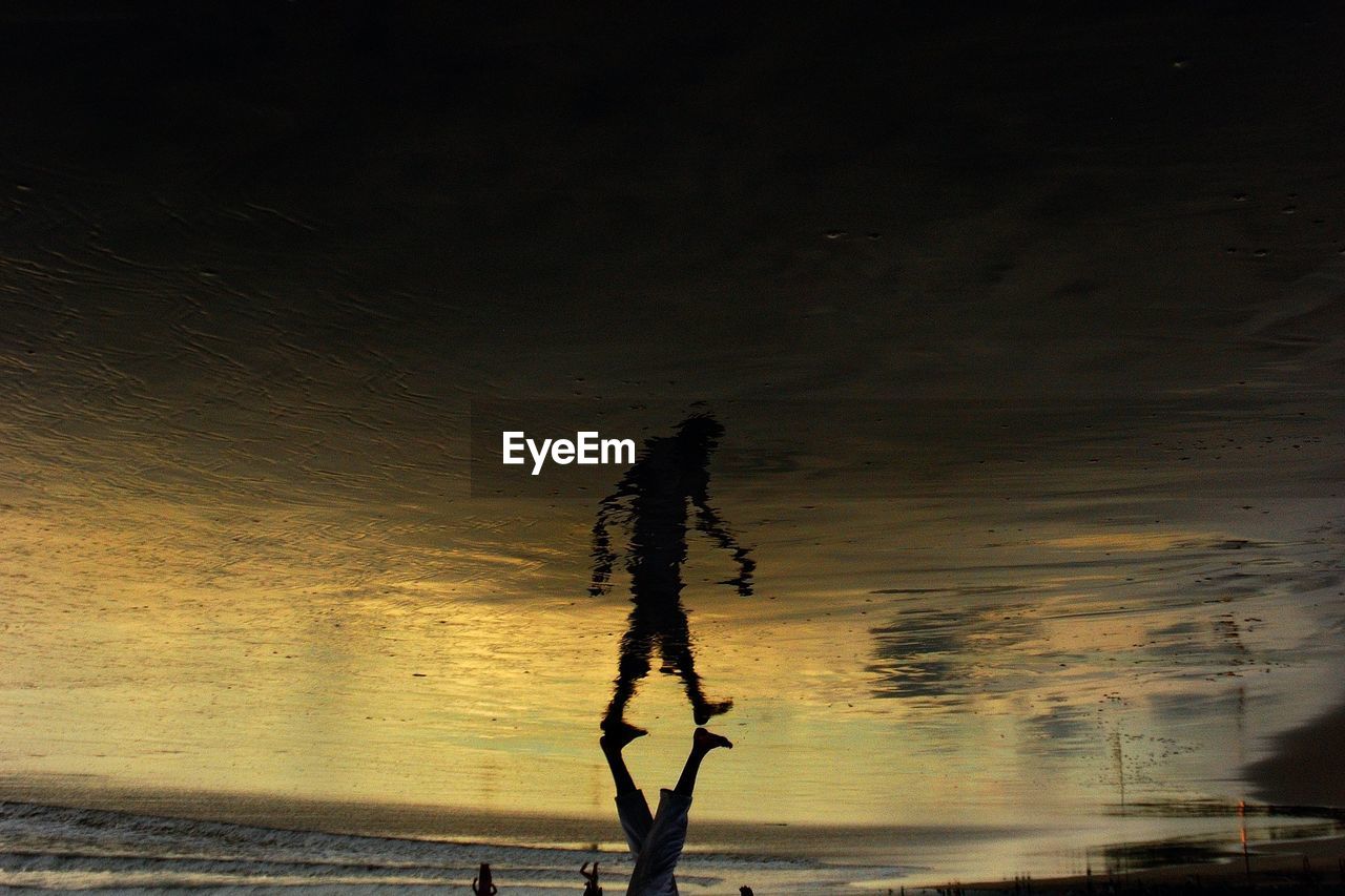 Upside down image of man walking on shore during sunset