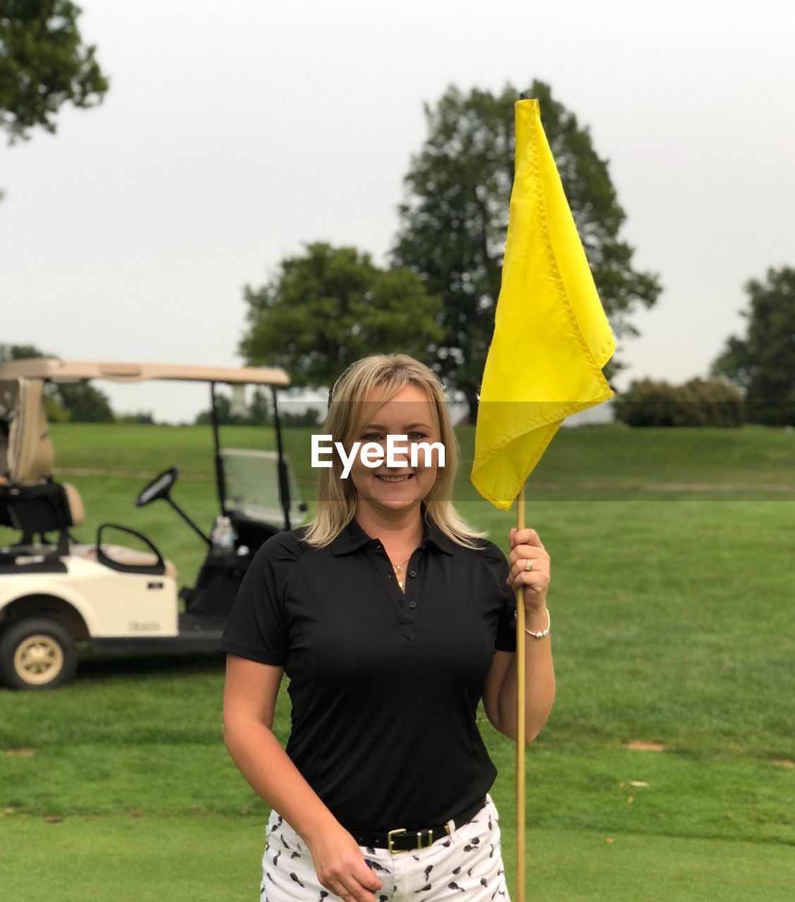Portrait of smiling woman holding yellow flag while standing on golf course