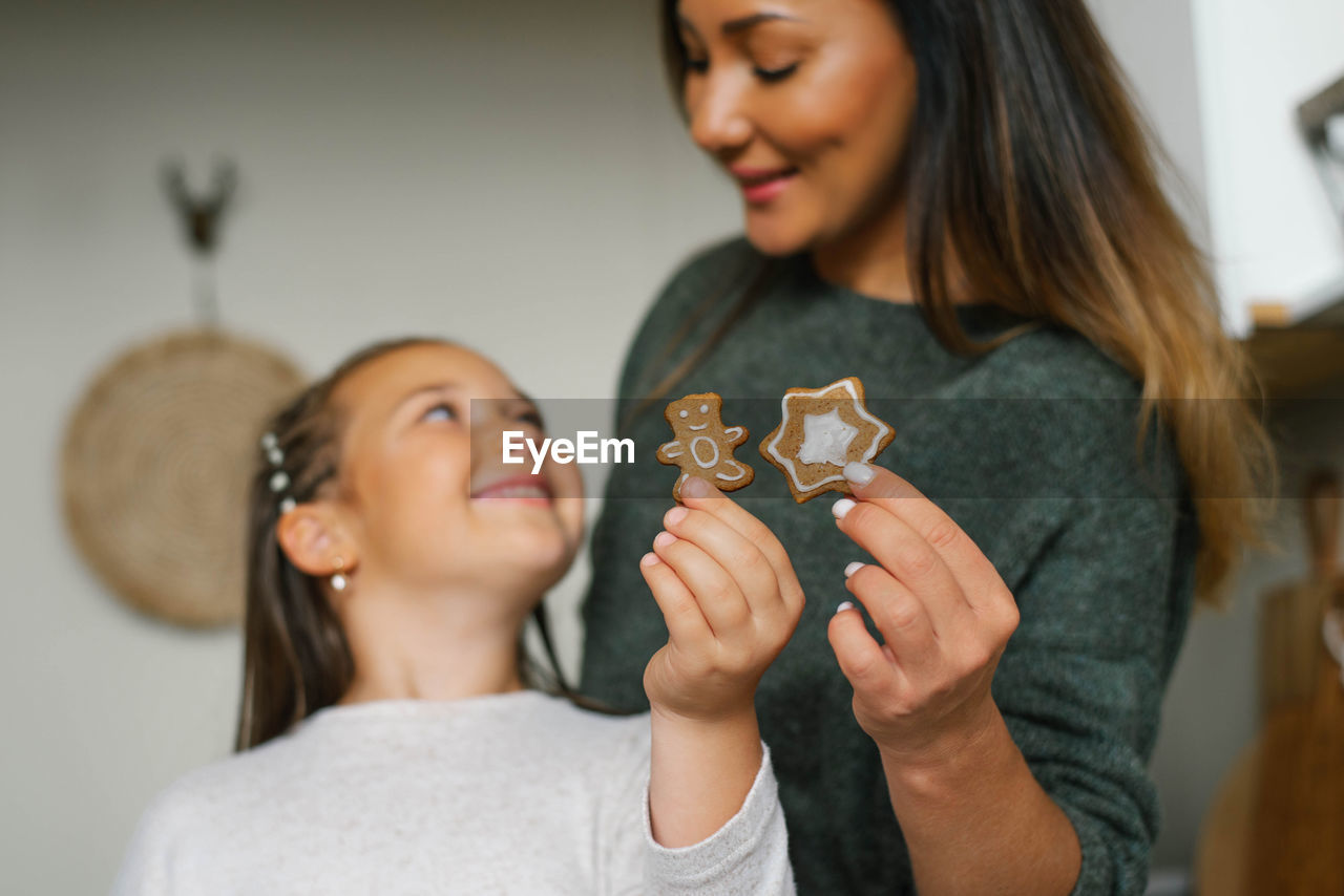 Smiling mom and her daughter are holding christmas cookies in their kitchen