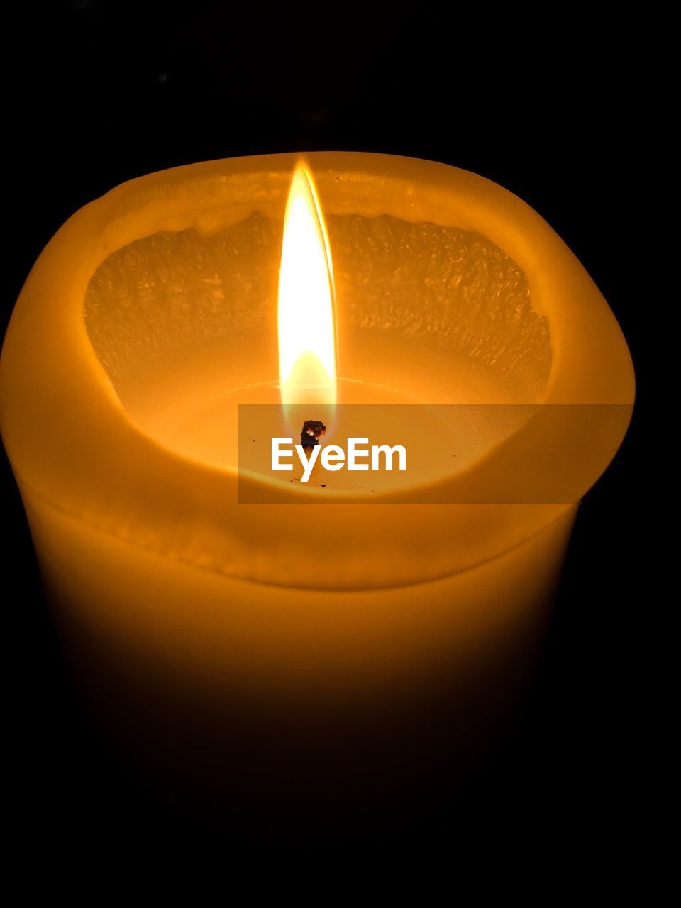 CLOSE-UP OF LIT CANDLE IN BLACK BACKGROUND