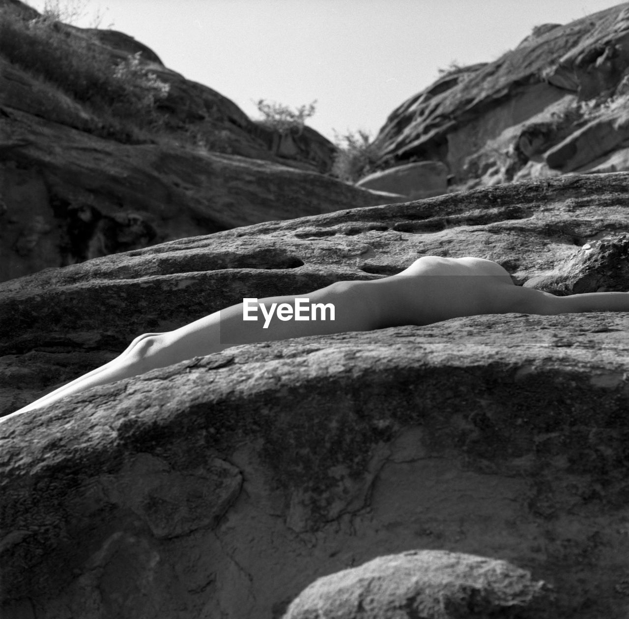 Shirtless woman lying on rock against sky