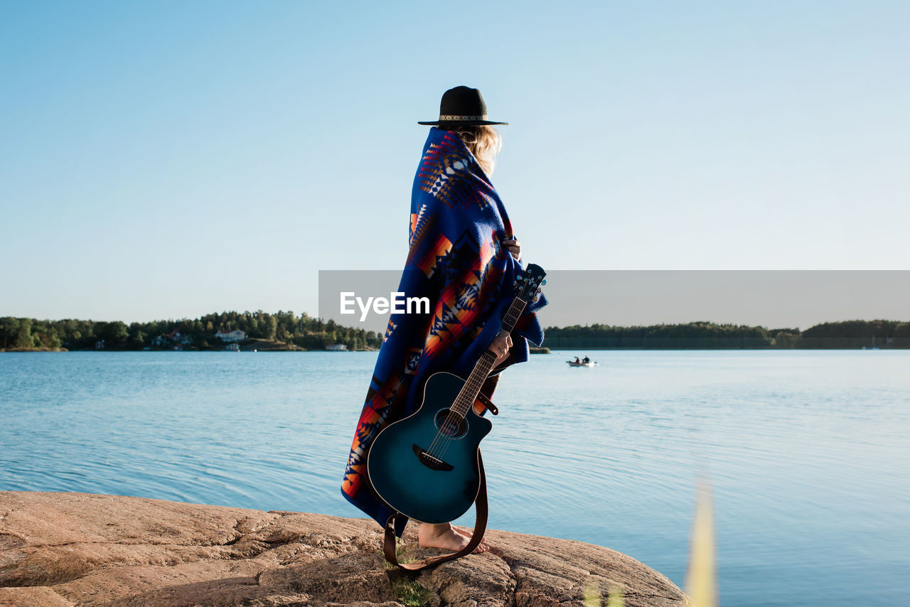 Woman stood wrapped in a pendleton blanket holding a guitar