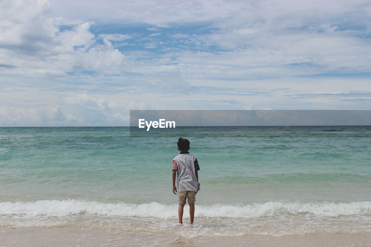 REAR VIEW OF WOMAN STANDING ON BEACH