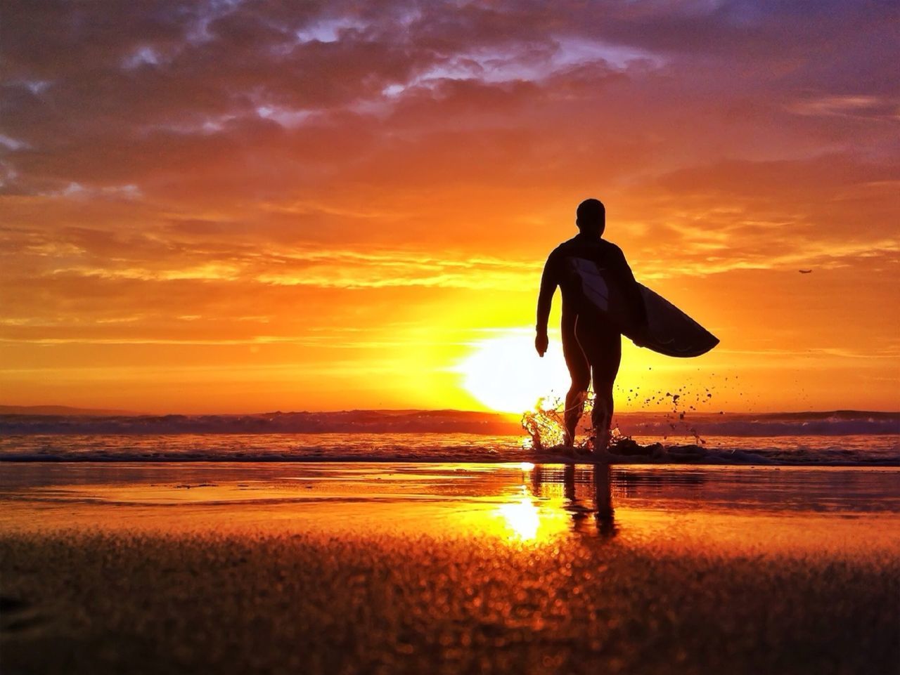 Silhouette man carrying surfboard on beach at sunset