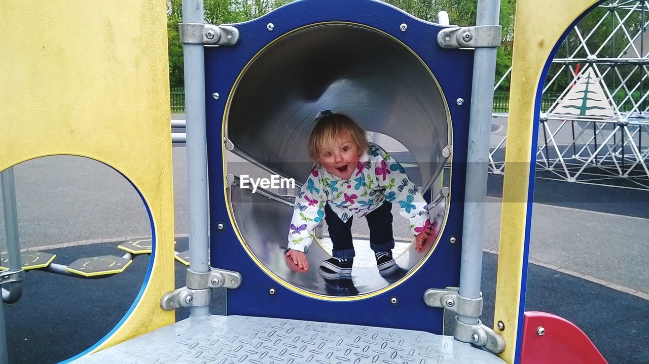 Portrait of happy girl playing on slide in playground