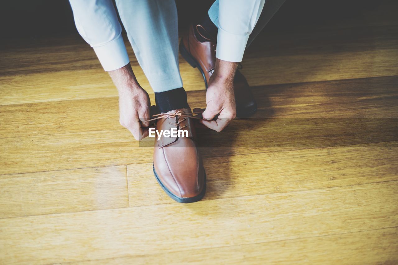 Low section of man tying shoelace on hardwood floor