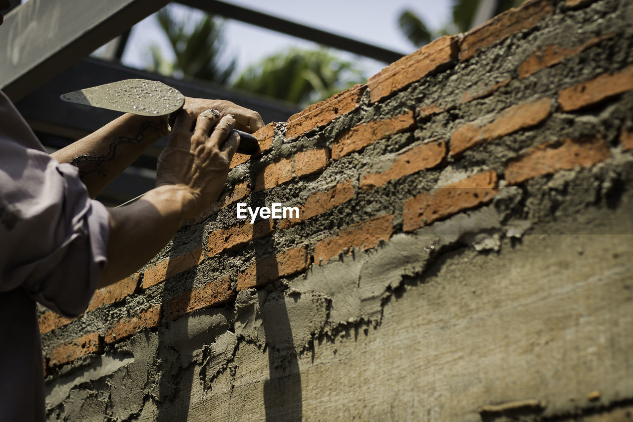 Cropped hands of man constructing brick wall