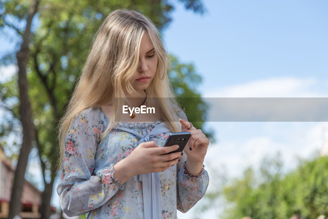 Young woman using mobile phone against sky