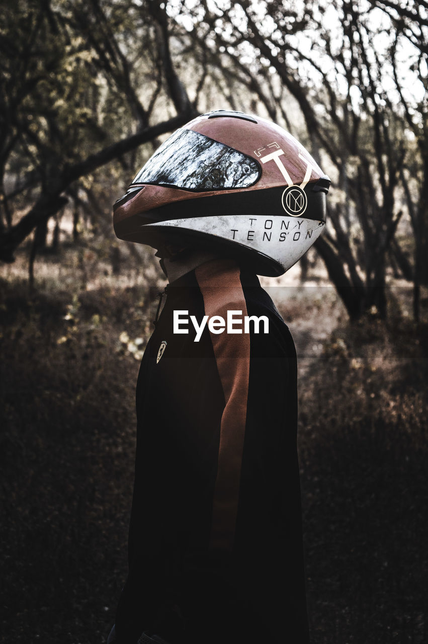 Side view of man wearing helmet while standing against trees in forest