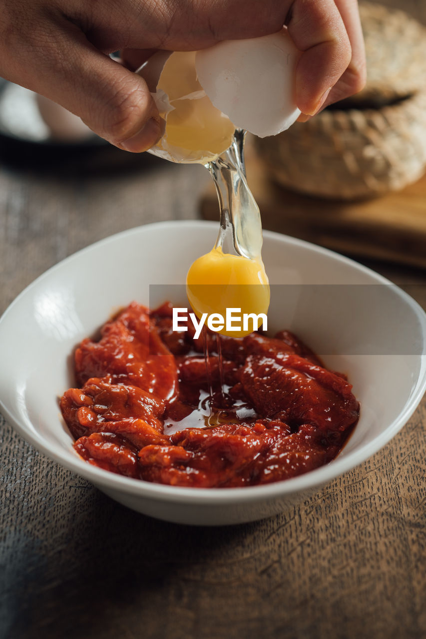 Cropped hand breaking egg in bowl