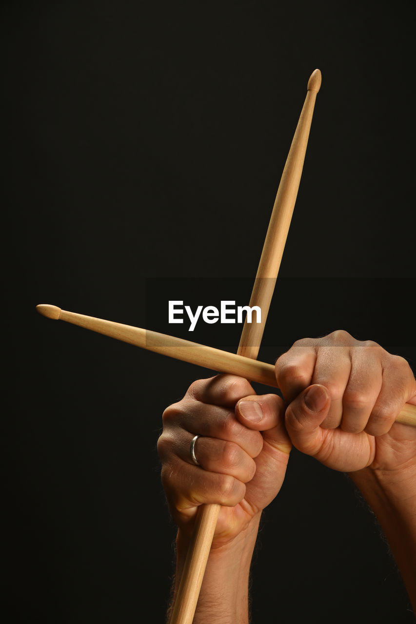 Cropped hand of musician holding drumsticks against black background