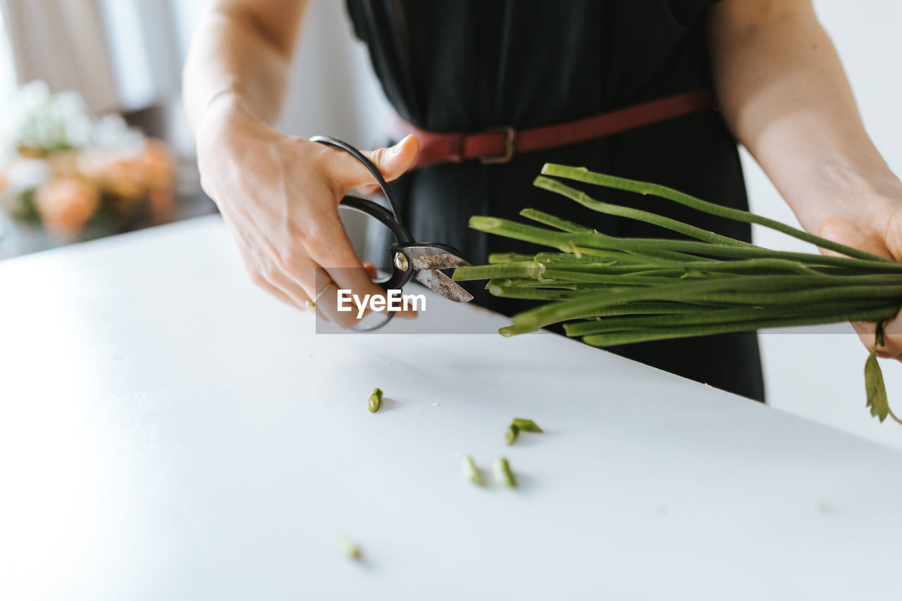 Midsection of florist cutting plant stems at table in shop