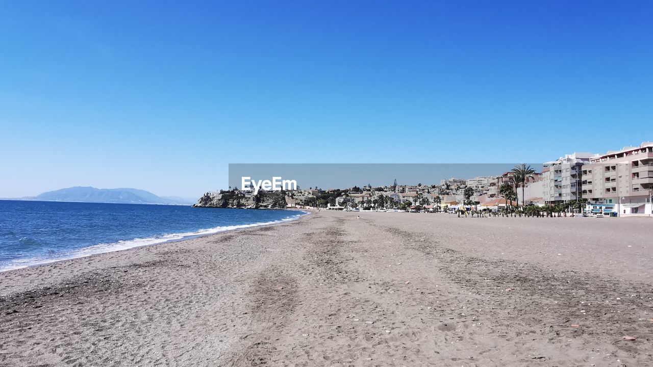 Scenic view of beach by city against clear blue sky