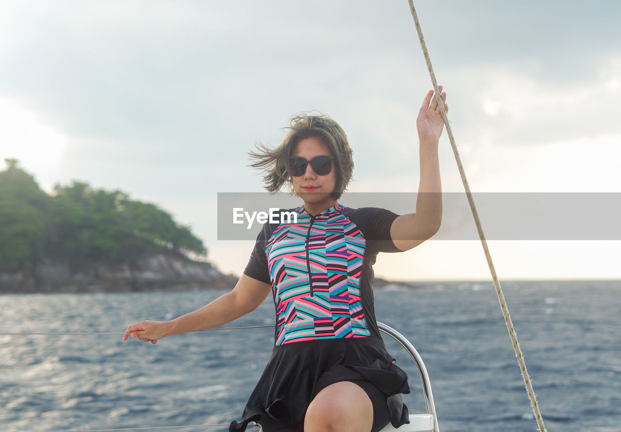 Portrait of young woman swinging at yatch against sky
