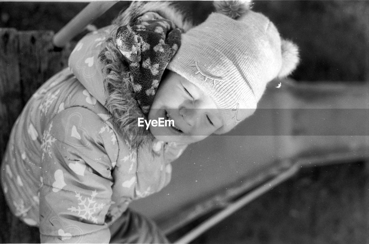 Girl with eyes closed sitting on footpath during winter