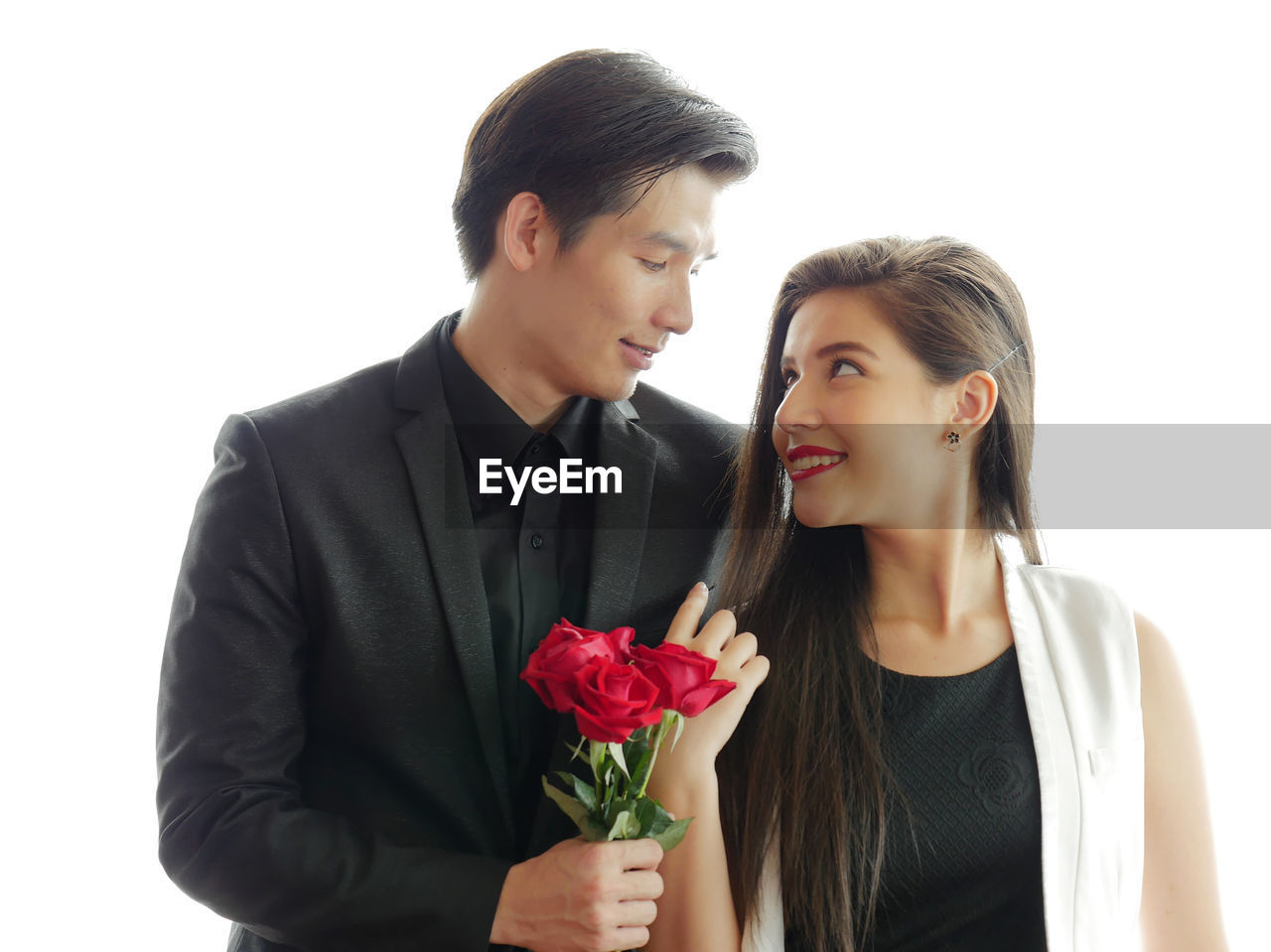 Smiling young couple with roses standing against white background