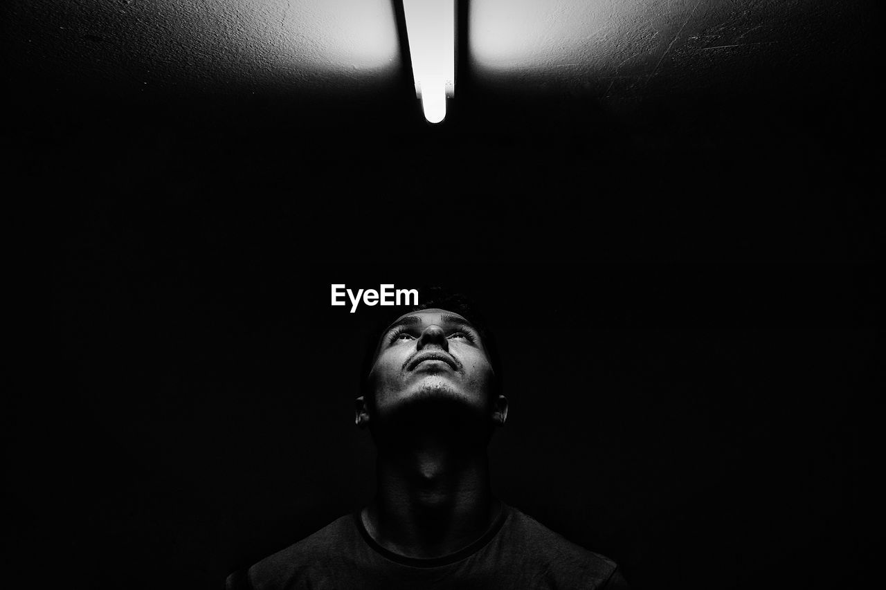 Young man looking towards fluorescent light on ceiling in darkroom