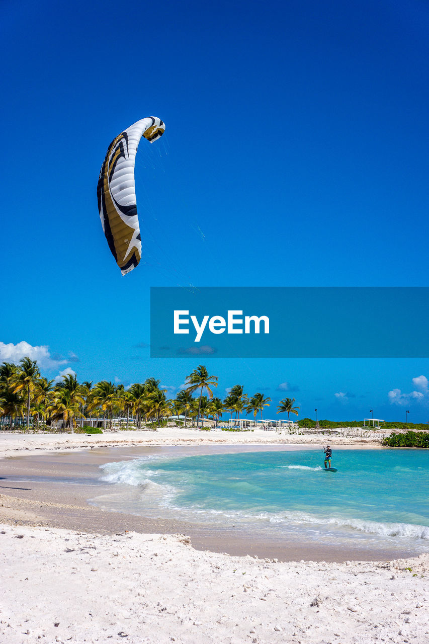 Man kiteboarding in sea against blue sky